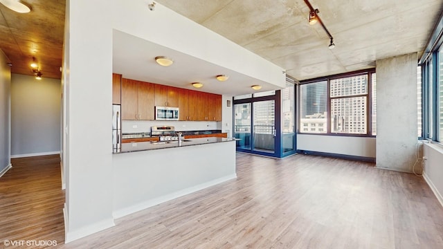 kitchen featuring brown cabinetry, light wood finished floors, a peninsula, stainless steel appliances, and dark countertops