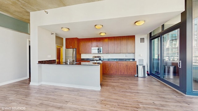 kitchen featuring light wood-type flooring, stainless steel appliances, brown cabinets, and a peninsula