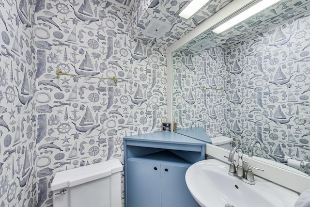 bathroom featuring wallpapered walls, toilet, and a sink