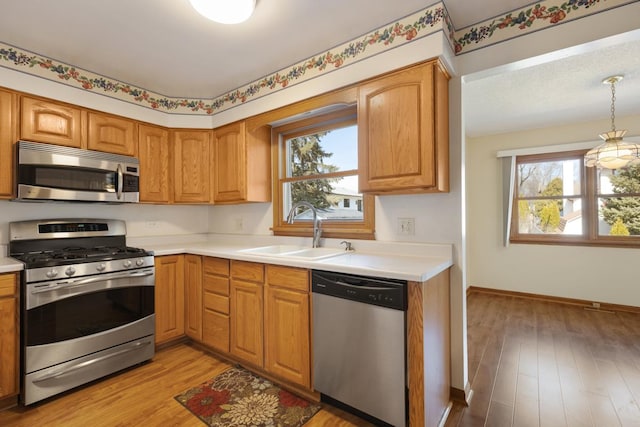 kitchen with stainless steel appliances, light countertops, light wood-style floors, and a sink