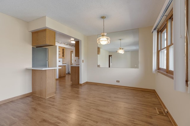 empty room with a ceiling fan, visible vents, baseboards, a textured ceiling, and light wood-type flooring