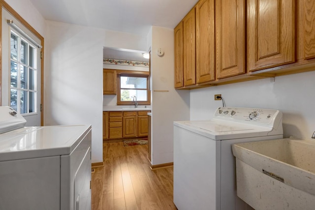 clothes washing area with washer and clothes dryer, cabinet space, light wood-style floors, and a sink