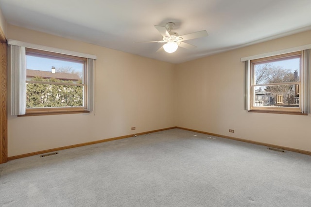 carpeted spare room with visible vents, plenty of natural light, and a ceiling fan