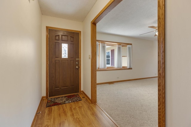 foyer entrance featuring baseboards, a textured ceiling, ceiling fan, and light wood finished floors