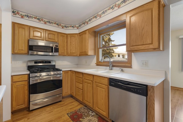 kitchen with a sink, stainless steel appliances, light wood-style floors, and light countertops