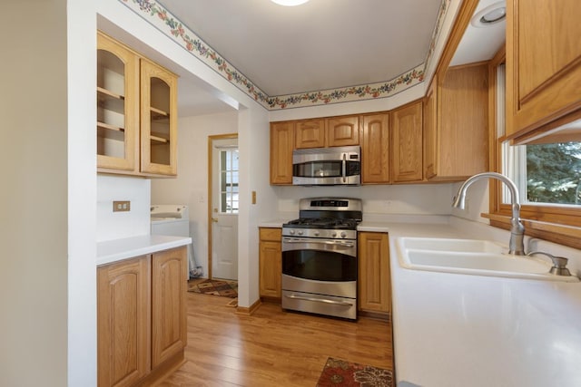 kitchen featuring glass insert cabinets, light countertops, light wood-style floors, stainless steel appliances, and a sink