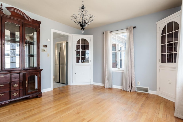 unfurnished dining area with visible vents, baseboards, light wood-style flooring, and a chandelier