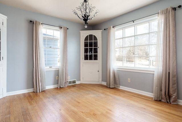 unfurnished dining area featuring light wood-type flooring, visible vents, baseboards, and a notable chandelier