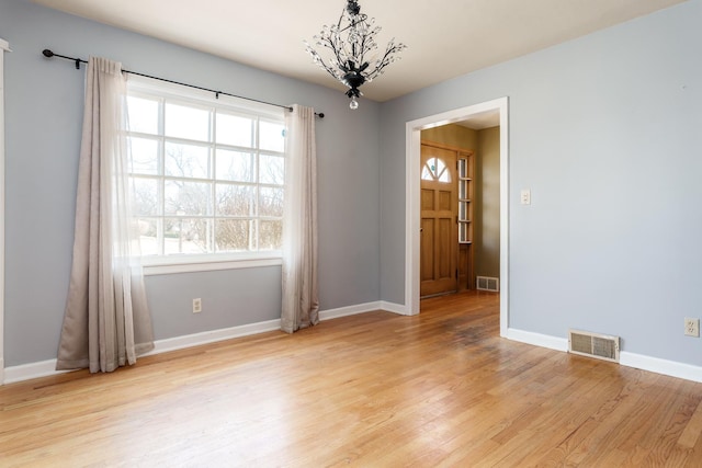 empty room featuring light wood-type flooring, baseboards, visible vents, and a chandelier