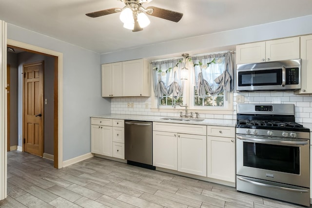 kitchen featuring wood tiled floor, ceiling fan, a sink, appliances with stainless steel finishes, and backsplash