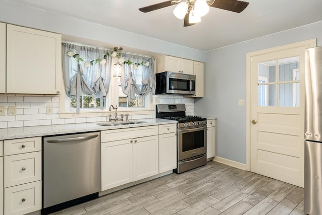 kitchen featuring a ceiling fan, light wood-style flooring, a sink, stainless steel appliances, and tasteful backsplash