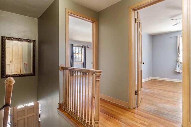 corridor featuring an upstairs landing, light wood-style flooring, and baseboards