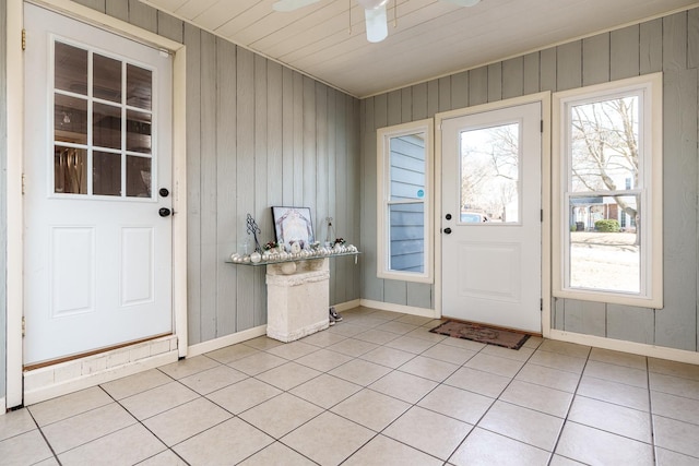 doorway with light tile patterned floors, plenty of natural light, ceiling fan, and wooden walls