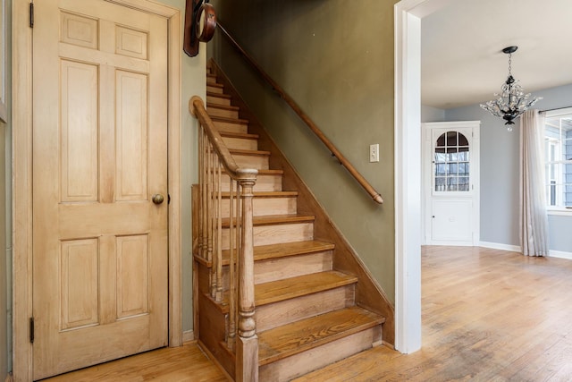 stairs featuring a notable chandelier, baseboards, and wood finished floors