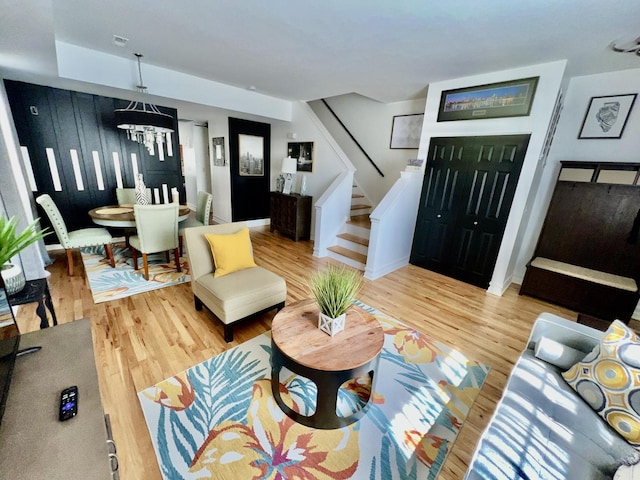 living area featuring stairway, a notable chandelier, wood finished floors, and baseboards