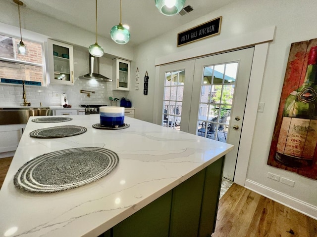 kitchen featuring decorative backsplash, hanging light fixtures, wall chimney exhaust hood, and light wood-style floors