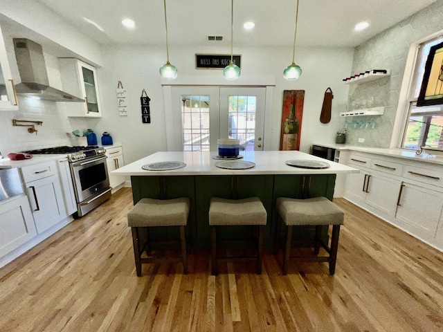 kitchen featuring open shelves, light wood-type flooring, wall chimney exhaust hood, and stainless steel gas range