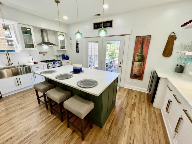 kitchen featuring a sink, white cabinets, light wood-style floors, stainless steel gas range oven, and wall chimney exhaust hood