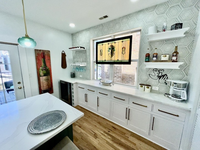 bar with visible vents, beverage cooler, pendant lighting, wood finished floors, and a bar