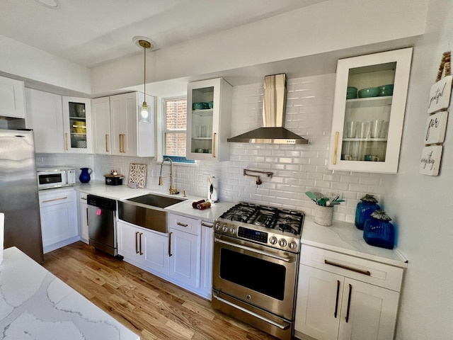 kitchen with a sink, tasteful backsplash, appliances with stainless steel finishes, wall chimney exhaust hood, and light wood finished floors