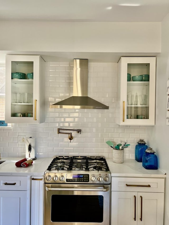 kitchen featuring glass insert cabinets, stainless steel range with gas stovetop, wall chimney exhaust hood, and white cabinets