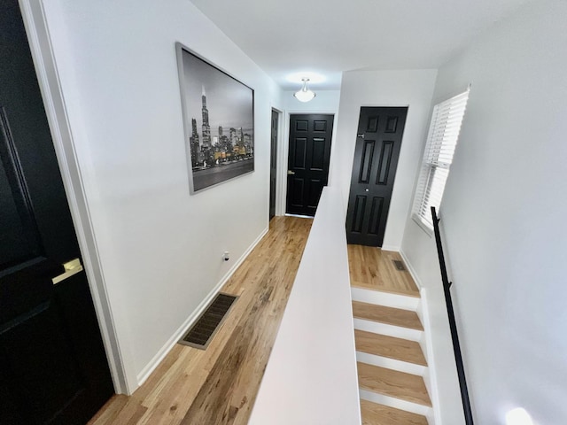 hall with visible vents, baseboards, wood finished floors, and stairway