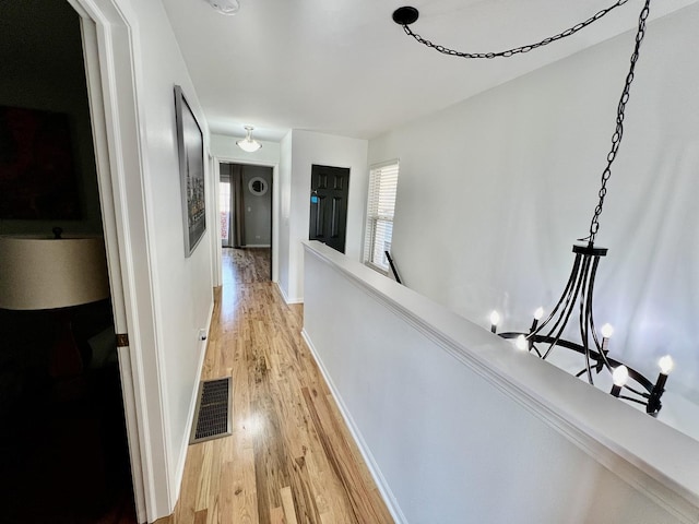 hall with visible vents, an upstairs landing, baseboards, and light wood finished floors