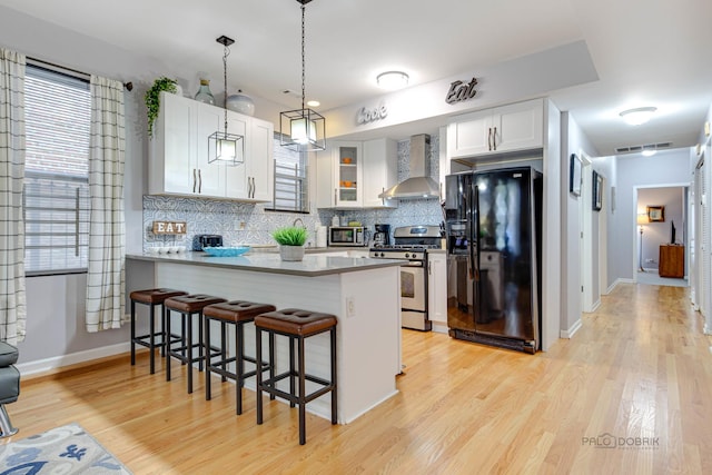 kitchen with a peninsula, wall chimney range hood, tasteful backsplash, and stainless steel appliances