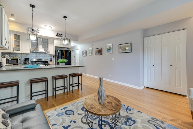 kitchen featuring visible vents, a breakfast bar, freestanding refrigerator, electric stove, and wall chimney exhaust hood