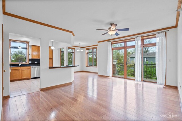unfurnished living room featuring light wood-type flooring, a sink, baseboards, ceiling fan with notable chandelier, and ornamental molding