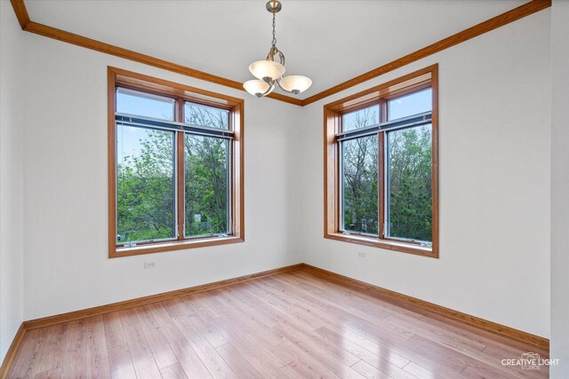 spare room with baseboards, a chandelier, ornamental molding, and light wood-type flooring