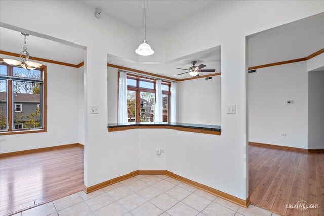 empty room with light wood-type flooring, baseboards, and ceiling fan with notable chandelier