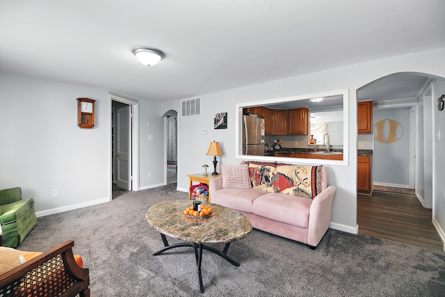 living room featuring visible vents, arched walkways, dark carpet, and baseboards