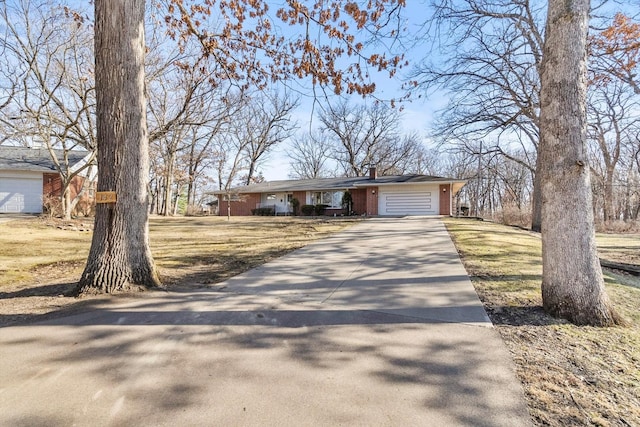 view of front facade with brick siding, a front lawn, concrete driveway, a chimney, and an attached garage