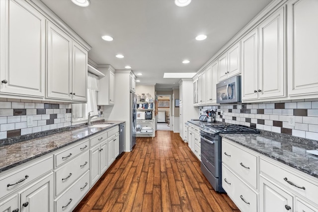 kitchen with a sink, backsplash, appliances with stainless steel finishes, white cabinets, and dark wood-style flooring