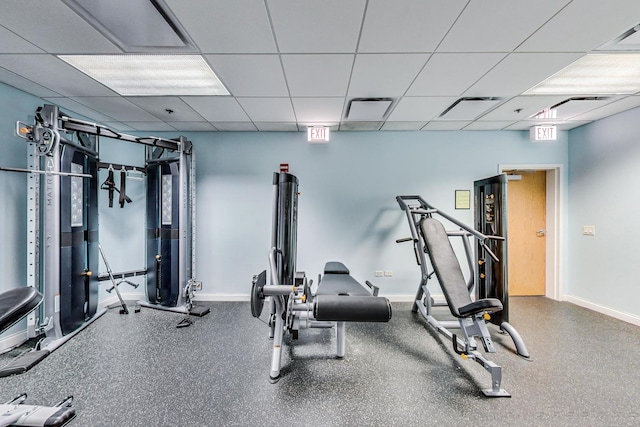 gym featuring a paneled ceiling and baseboards