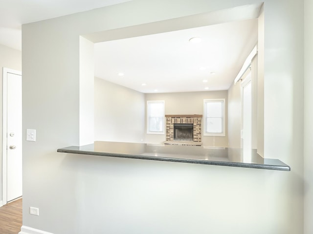 kitchen featuring wood finished floors, baseboards, recessed lighting, dark countertops, and a brick fireplace