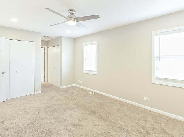 unfurnished bedroom featuring recessed lighting, light colored carpet, two closets, and baseboards