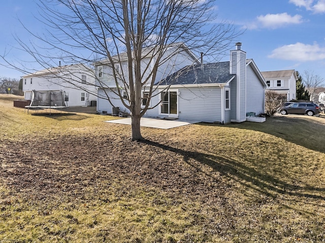 view of side of property featuring a patio, a trampoline, a yard, and a chimney