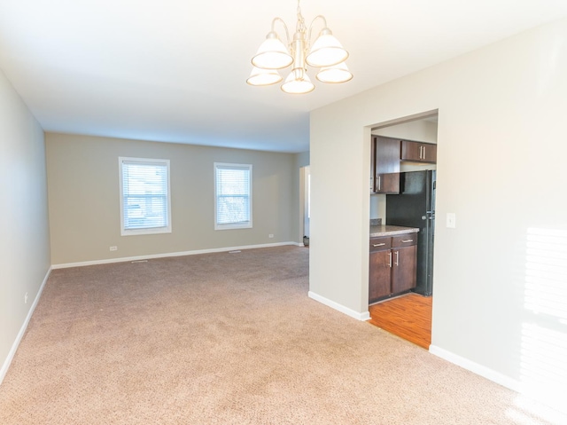 spare room with baseboards, light carpet, and a notable chandelier