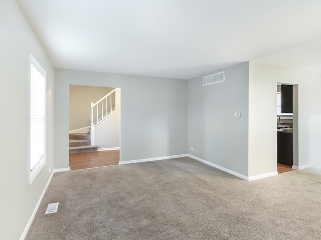 empty room featuring visible vents, carpet flooring, and stairway