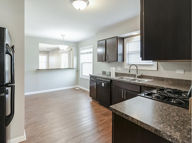 kitchen featuring baseboards, a sink, black appliances, light wood-style floors, and dark countertops