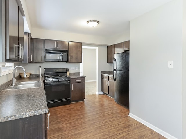 kitchen with baseboards, dark wood-style flooring, a sink, black appliances, and dark brown cabinets