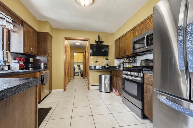 kitchen featuring dark countertops, a sink, light tile patterned flooring, stainless steel appliances, and a baseboard radiator