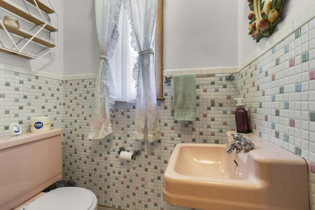 bathroom with a sink, toilet, and tile walls