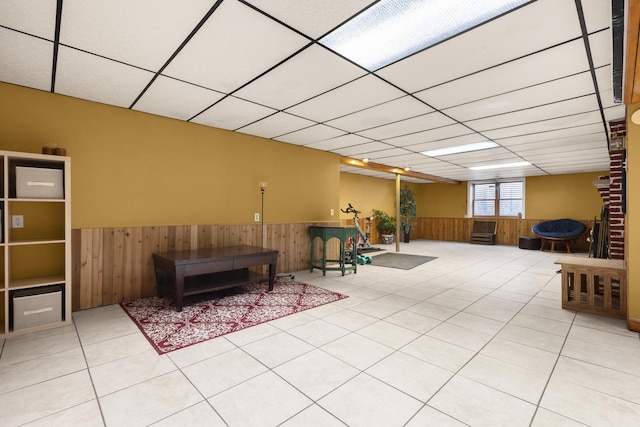 living area with a paneled ceiling, wood walls, and wainscoting