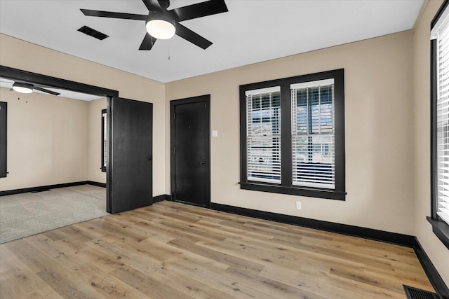 empty room with baseboards, a ceiling fan, visible vents, and light wood-type flooring