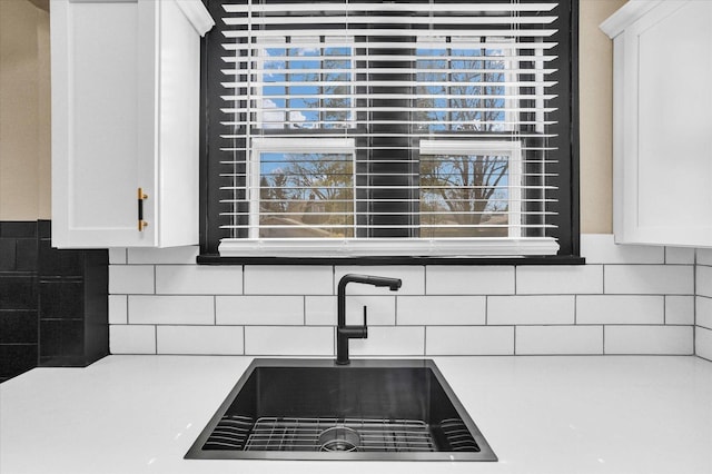 interior details with decorative backsplash, white cabinetry, light countertops, and a sink