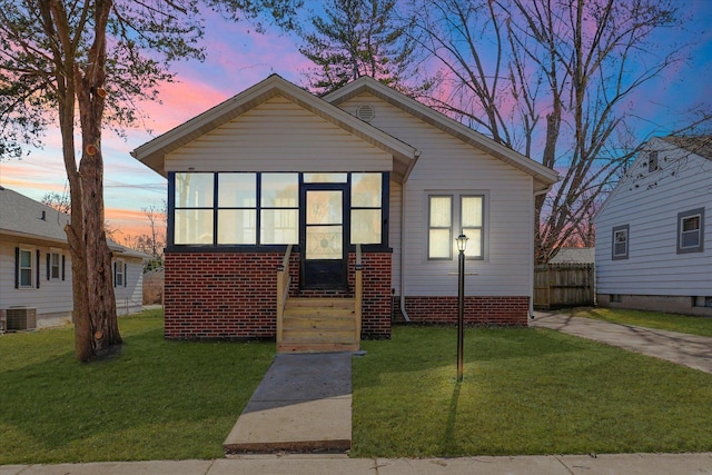 bungalow-style home with central AC unit, fence, a yard, and a sunroom