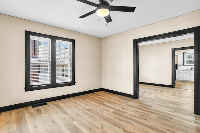 unfurnished room featuring light wood finished floors, visible vents, baseboards, and a ceiling fan